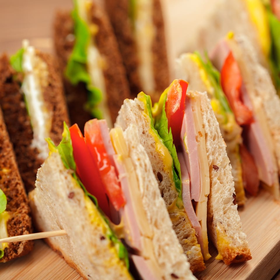 Close-up of deli sandwiches with various fillings, including ham, cheese, lettuce, and tomato.