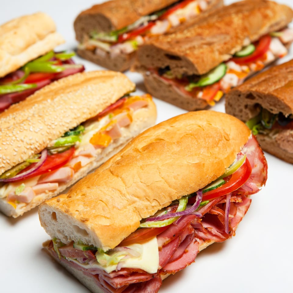 Several deli sandwiches with various meats, cheeses, and vegetables on different breads.